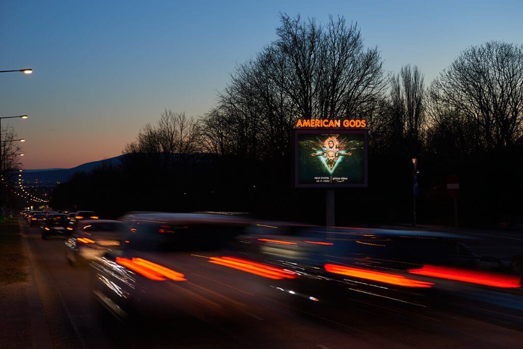 Leuchtreklame auf befahrener Straße Abends